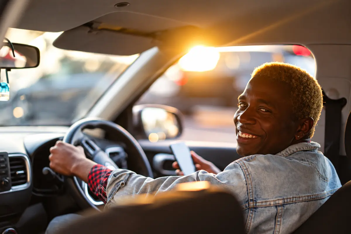 A driver smiling over his shoulder in a sunlit car