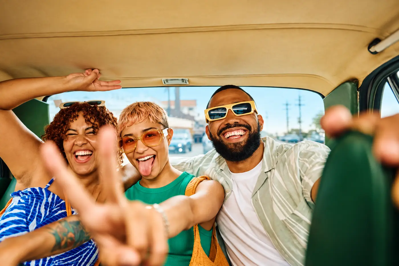 Three friends laughing in the back of a car, one making a peace sign