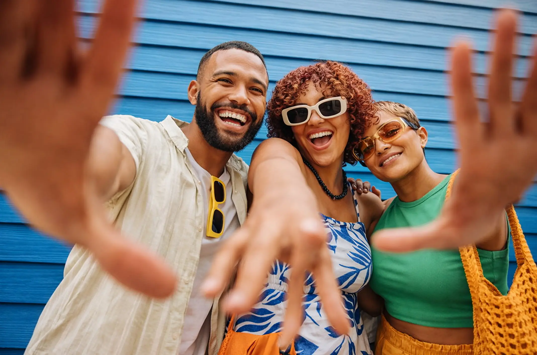 Three friends laughing and reaching towards the camera in front of a blue wall