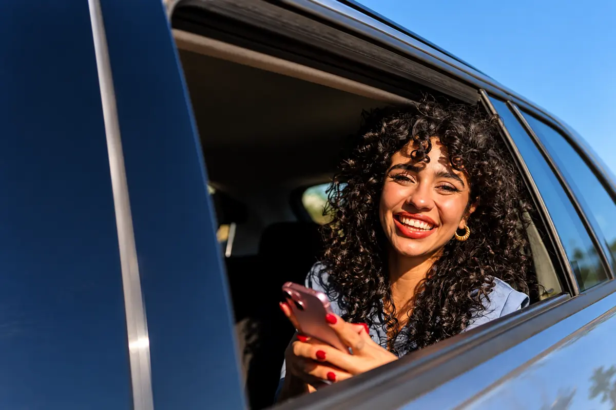 A rider smiling out of a car window with her phone in her hand